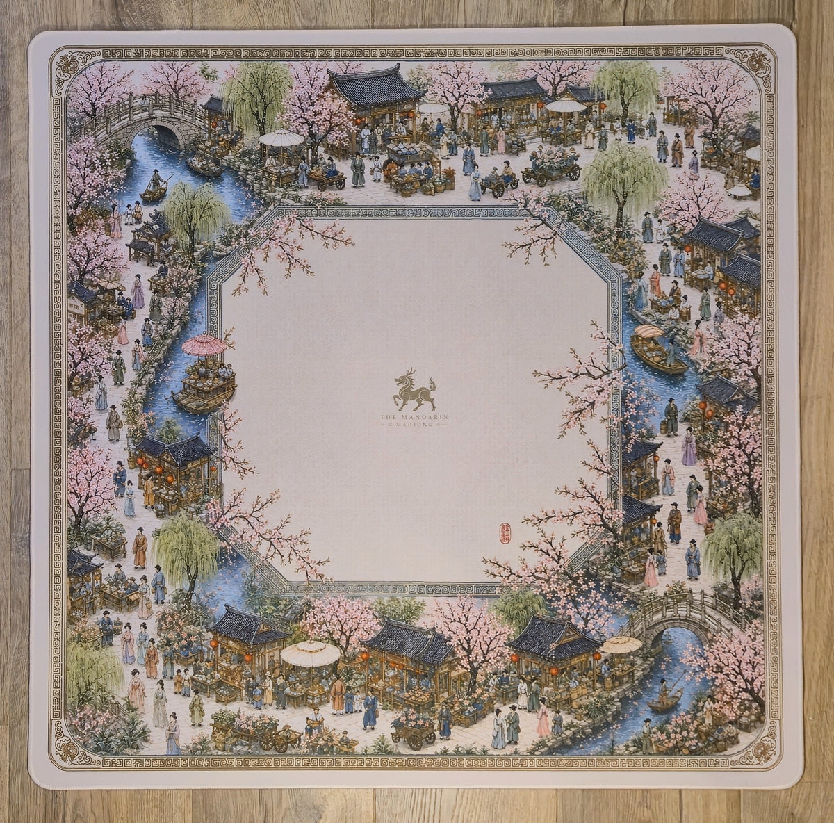 A square decorative mat or plate featuring an ornate traditional Chinese landscape illustration with pink cherry blossoms, water channels, pavements, and small figures
