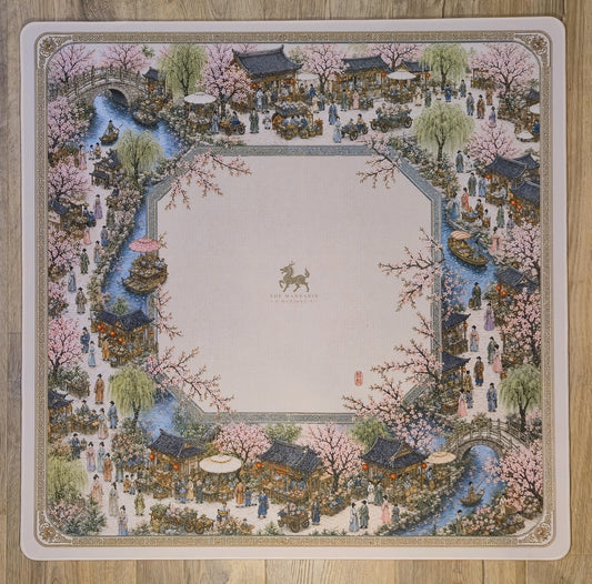 A square decorative mat or plate featuring an ornate traditional Chinese landscape illustration with pink cherry blossoms, water channels, pavements, and small figures